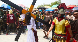 Devotee drags a massive cross next to someone dressed as a Roman soldier